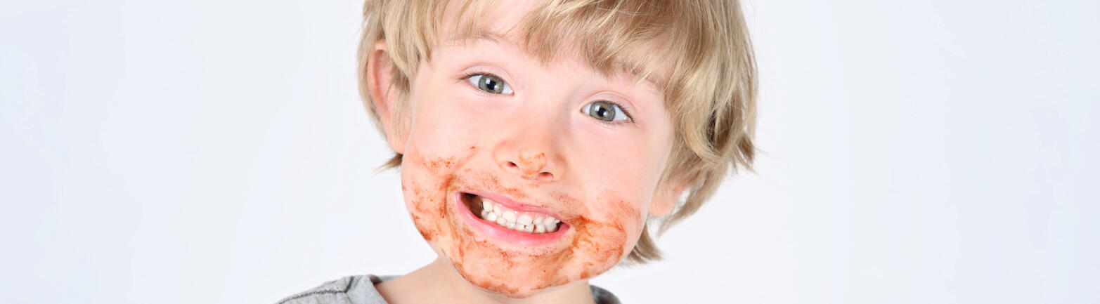 Young child holding unwrapped chocolate bar looking at camera with chocolate residue around mouth.