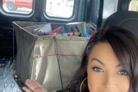 Woman gesturing over her right shoulder at a mail cart full of boxed toys for children.