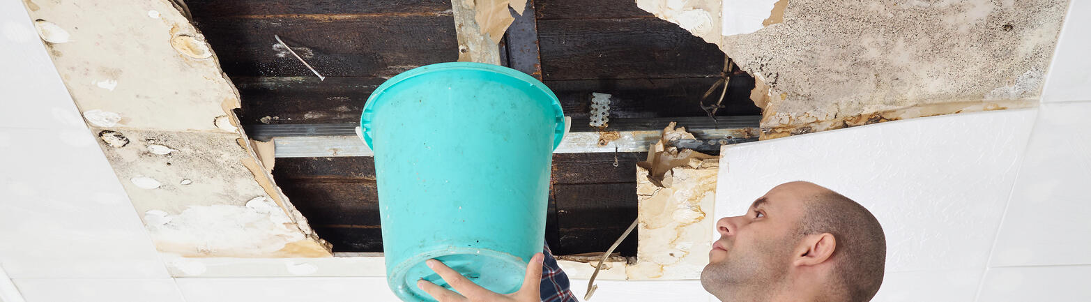 Man holding a bucket under water damaged ceiling